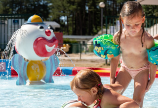 Twee kinderen met zwembandjes spelen in het kinderbad bij een lodge, met een clownfontein op de achtergrond.