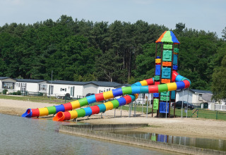Scivolo colorato su una spiaggia di un lodge, con bungalow e alberi sullo sfondo, giornata soleggiata.