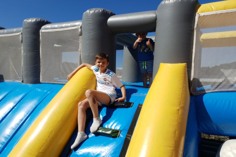 Twee kinderen spelen op een grote, kleurrijke opblaasbare glijbaan buiten bij een lodge in de zon.