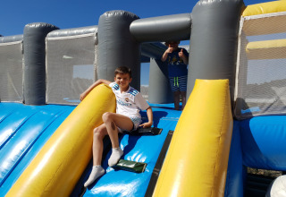 Twee kinderen spelen op een grote, kleurrijke opblaasbare glijbaan buiten bij een lodge in de zon.