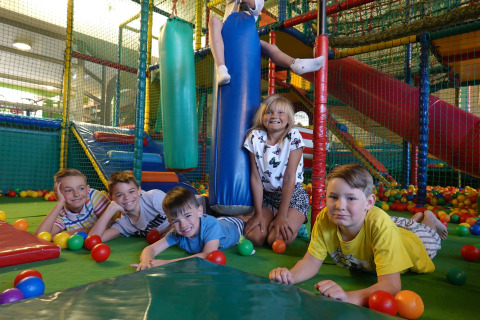 Bambini che giocano in un'area giochi interna colorata con piscina di palline e scivoli in un lodge.