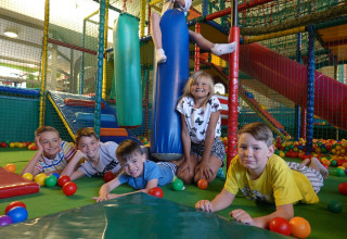 Bambini che giocano in un'area giochi interna colorata con piscina di palline e scivoli in un lodge.