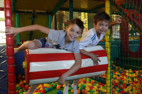 Twee lachende jongens spelen samen op een zachte rol boven kleurrijke ballen in een lodge-speelruimte.