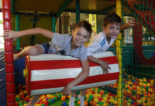 Twee lachende jongens spelen samen op een zachte rol boven kleurrijke ballen in een lodge-speelruimte.