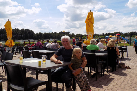 Un uomo e un bambino siedono insieme nel cortile esterno di un lodge, con un parco giochi sullo sfondo.