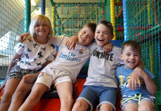 Vier lachende kinderen zitten samen in een kleurrijke binnenspeeltuin in een lodge.