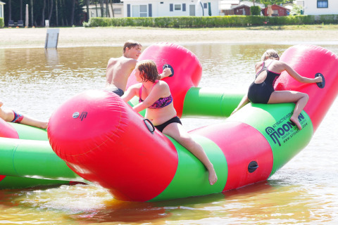 Kinderen spelen op een groot opblaasbaar waterobject bij een lodge aan het meer op een zonnige dag.