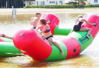 Kinderen spelen op een groot opblaasbaar waterobject bij een lodge aan het meer op een zonnige dag.