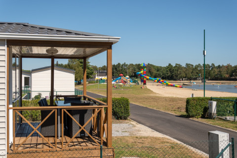 Uitzicht vanaf een lodge veranda op een strand, speeltuin en kleurrijke glijbaan bij een meer.
