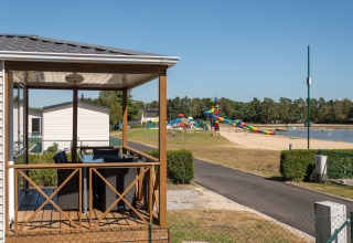 Uitzicht vanaf een lodge veranda op een strand, speeltuin en kleurrijke glijbaan bij een meer.