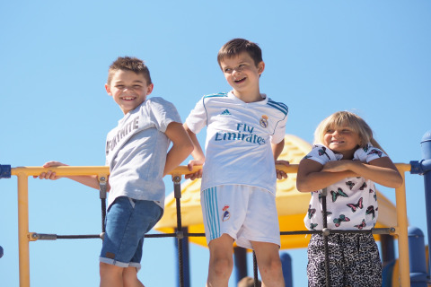 Drie lachende kinderen staan op een speeltoestel en genieten van een zonnige dag bij de lodge in de openlucht.