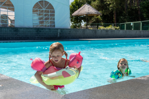 Due bambini giocano in piscina con braccioli e salvagente presso Verblijfpark Breebos 4 in Belgio.