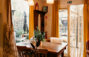 Acogedor comedor en el Chalet «Chocolat» en Bélgica, con mesa de madera, cortinas amarillas y plantas.
