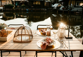 Mesa al aire libre junto al agua en Chalet «Chocolat», Bélgica, puesta para dos personas con vajilla elegante.