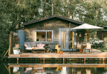 Chalet Chocolat, una cabaña de madera junto al lago con terraza, muebles de exterior y vegetación frondosa.