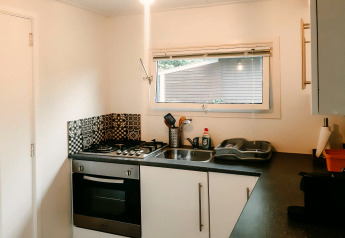 Cocina compacta en el Chalet «Chocolat» en Bélgica con estufa de gas, horno, fregadero y ventana sobre la encimera.