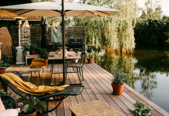 Terraza de madera con sillas, sombrilla y plantas junto al agua en el Chalet «Chocolat» en Bélgica.