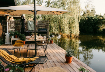 Terraza junto al lago en Chalet «Chocolat» en Bélgica, con sombrilla, mesas y vistas al agua.