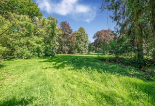 Photo of a lush green lawn with surrounding trees and a blue sky, taken at a chalet on a sunny day.