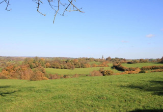 View from a chalet overlooking green fields, autumn trees, and a clear blue sky in the distance.