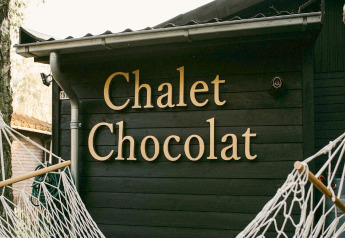 Foto de un chalet de madera oscuro con el letrero 'Chalet Chocolat' en Bélgica, enmarcado por hamacas.