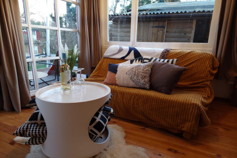 Acogedora sala en Casita La Luna, Bélgica, con sofá, cojines, mesa redonda y botella de vino.