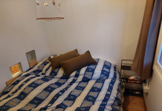 Dormitorio en chalet Casita La Luna en Bélgica con cama doble, cojines marrones y ventana con cortina.