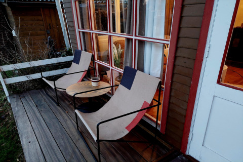 Terraza de madera en Casita La Luna, Bélgica, con dos sillas, una mesa redonda y luces acogedoras dentro.