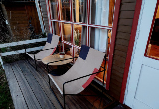 Terraza de madera en Casita La Luna, Bélgica, con dos sillas, una mesa redonda y luces acogedoras dentro.