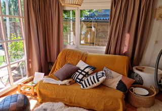 Acogedora sala en Casita La Luna, Bélgica, con sofá amarillo, cojines y ventanas grandes al jardín.