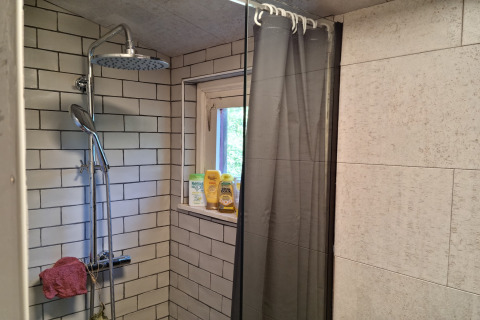 Ducha con azulejos grises y ventana en Casita La Luna, Bélgica, con productos de baño en la repisa.