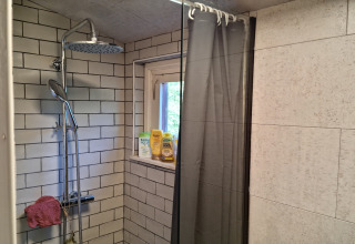 Ducha con azulejos grises y ventana en Casita La Luna, Bélgica, con productos de baño en la repisa.