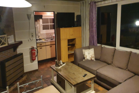 Living room with sectional sofa, TV, fireplace, and view into kitchen at 'The Deer Forest' lodge in Belgium.