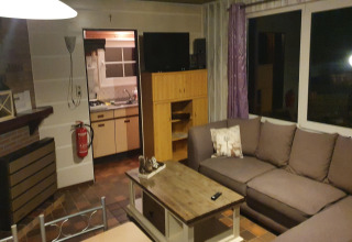 Living room with sectional sofa, TV, fireplace, and view into kitchen at 'The Deer Forest' lodge in Belgium.