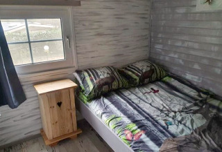 Knusse slaapkamer in The Deer Forest lodge in België met bosdieren motief en houten kastje naast het bed.