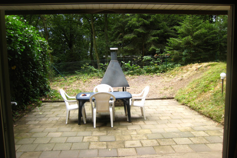 Patio con sedie bianche, tavolo nero e barbecue, immerso nella foresta a The Deer Forest, Belgio.