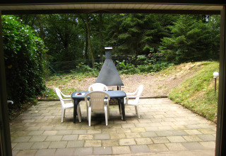 Patio con sedie bianche, tavolo nero e barbecue, immerso nella foresta a The Deer Forest, Belgio.