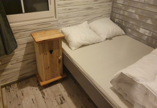 Et hyggeligt soveværelse i The Deer Forest lodge i Belgien med trævægge, dobbeltseng og natbord.