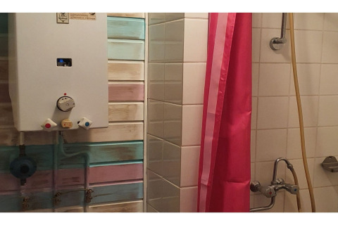Bathroom at The Deer Forest lodge in Belgium showing a shower, water heater, and pink shower curtain.