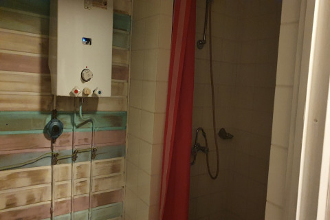 Chauffe-eau et douche avec rideau rouge dans la salle de bain au lodge The Deer Forest en Belgique.