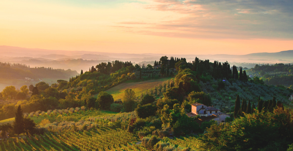 Heuvels en wijngaarden rond Siena, Toscane, Italië bij zonsondergang, met een huis omringd door groen.