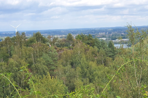 Vista da un lodge su colline verdi con alberi, turbina eolica e una città in lontananza sotto il cielo nuvoloso.