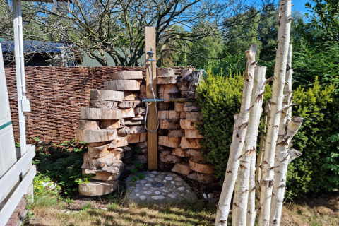 Ducha exterior en el chalet 'Casita La Luna' en Bélgica, rodeada de troncos de madera y vegetación.