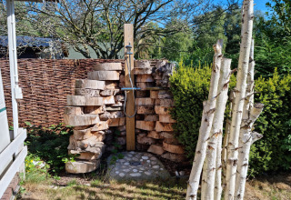Ducha exterior en el chalet 'Casita La Luna' en Bélgica, rodeada de troncos de madera y vegetación.