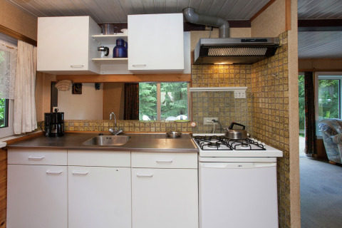 Cocina compacta en Forest House the Squirrel, Bélgica, con estufa, fregadero y gabinetes blancos modernos.