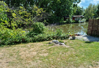 Vista de un jardín verde junto al agua en el chalet Casita La Luna en Bélgica, con árboles y cabaña roja.