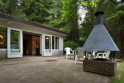 Terraza del Forest House the Squirrel en Bélgica con chimenea exterior, sillas y bosque alrededor.