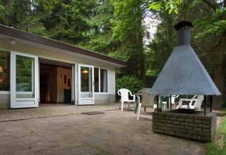 Terraza del Forest House the Squirrel en Bélgica con chimenea exterior, sillas y bosque alrededor.