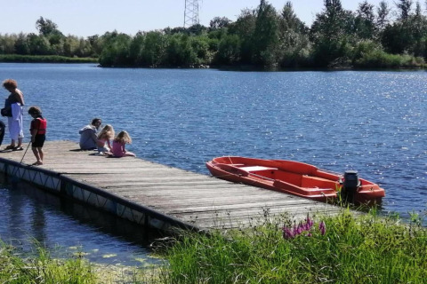 Famille se détend sur un ponton en bois avec un bateau rouge à Forest House the Squirrel en Belgique.