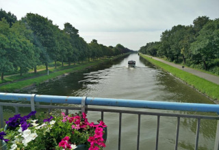 Vue d’un pont fleuri sur une rivière, un bateau et des arbres verts, prise dans un hébergement glamping.